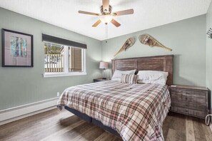 Une chambre à coucher avec un lit, un ventilateur de plafond, une fenêtre et une table de chevet.