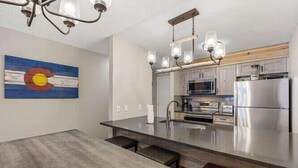 A modern kitchen with a large island, stainless steel appliances, and a hanging light fixture.