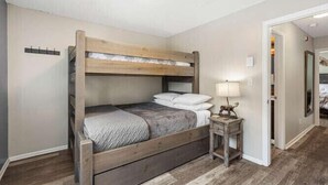 A bedroom with a wooden bunk bed, a bedside table with a lamp, and a mirror on the wall.