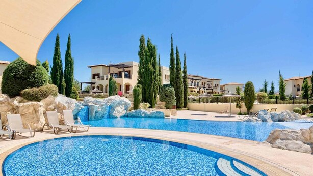 A resort pool area with a clear blue pool, lounge chairs, and a waterfall feature.