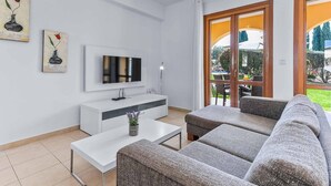 A modern living room with a flat-screen TV, white console, grey sofa, and a small table with a plant.