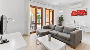 A modern living room with a grey sectional sofa, a white coffee table, a TV, and a dining area with white chairs.