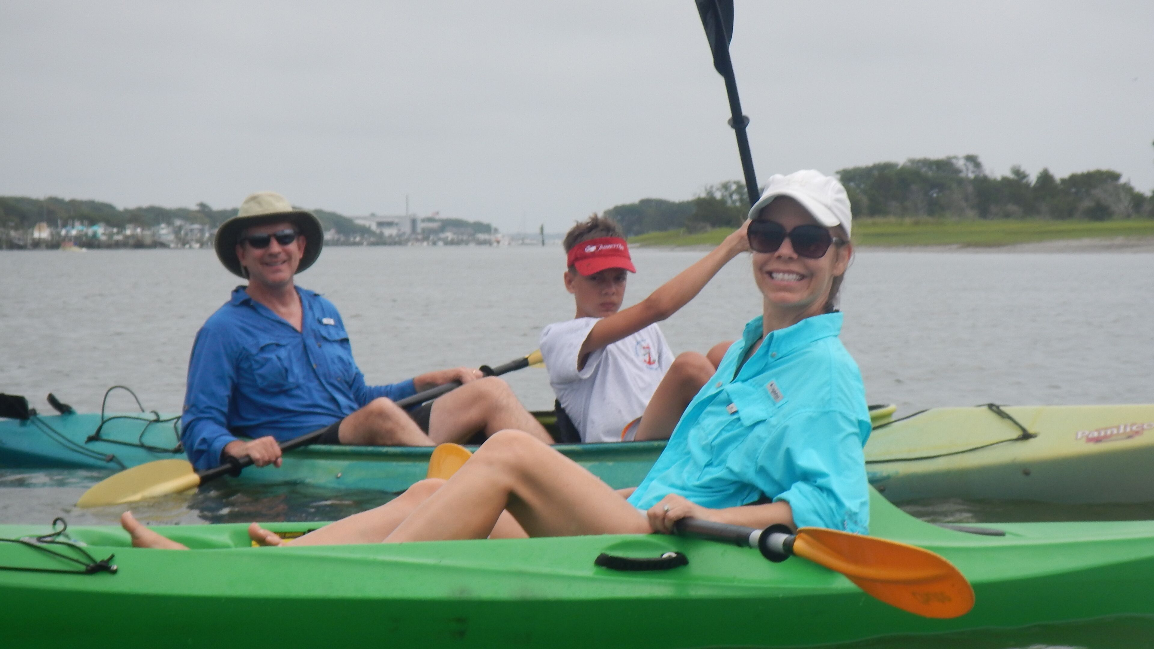 Tres personas en un kayak verde sobre el agua.