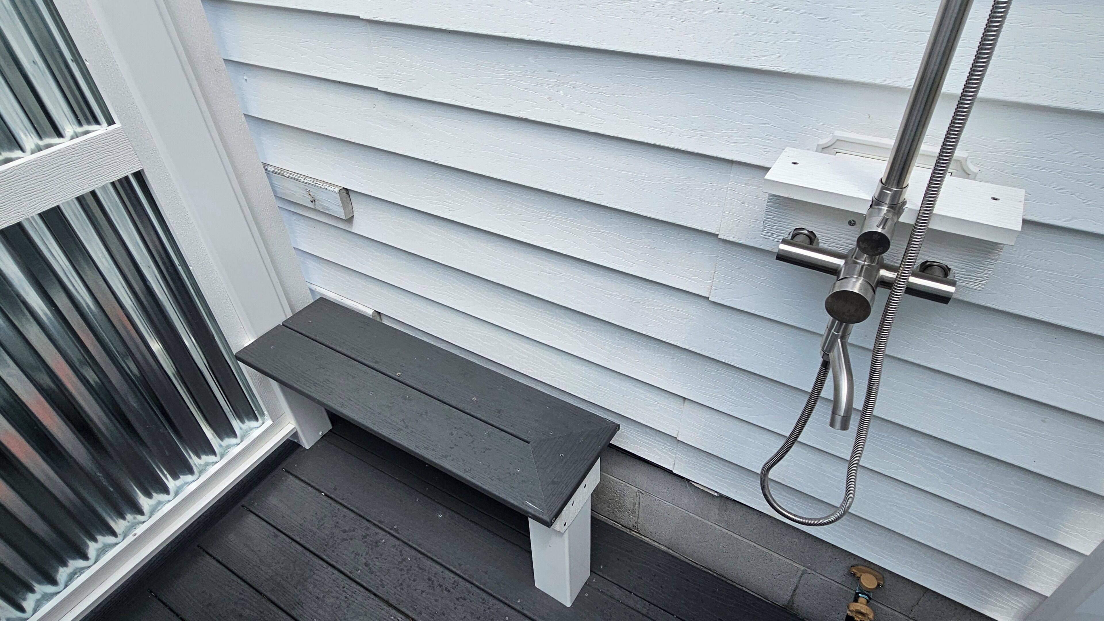 Un banc en bois se trouve devant une maison, qui est dotée d’une rambarde en métal et d’un tuyau fixé au mur.