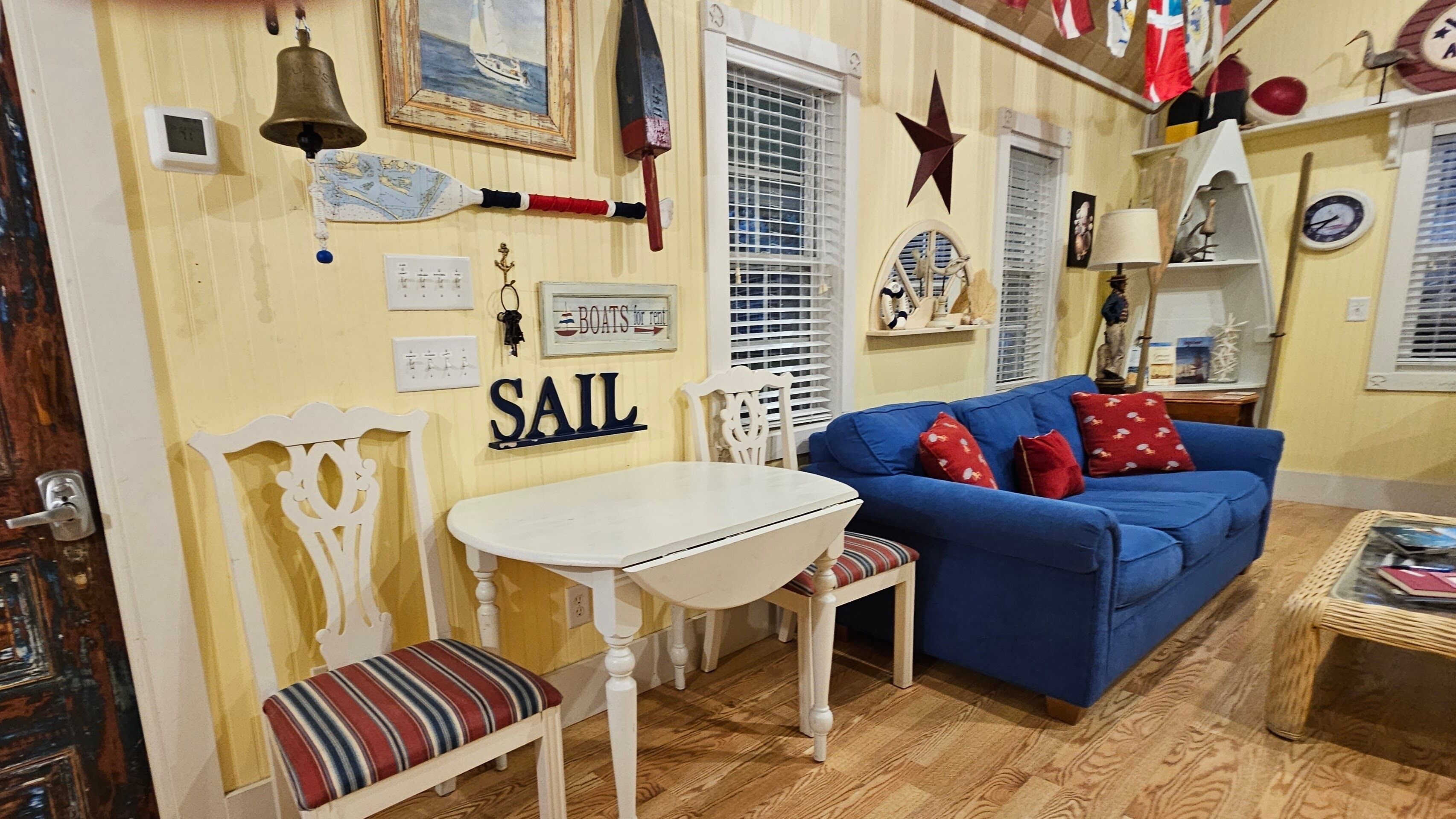 A cozy room with a blue sofa, a white table, and a bench. A sign on the wall reads "SAIL".