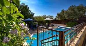 Una piscina con cubierta de madera y sillas reclinables, rodeada de follaje y árboles.