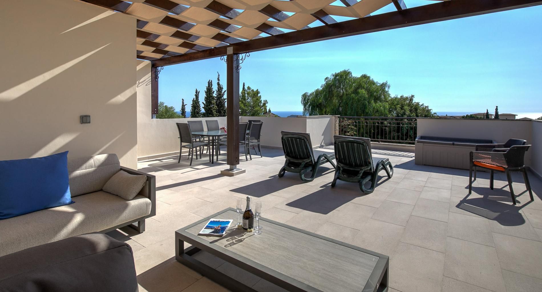 A sunlit outdoor patio with a sofa, chairs, a table, and a pergola.