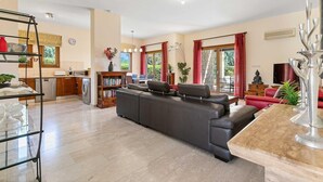 A modern living room with a black leather sofa, a glass coffee table, and a bookshelf.