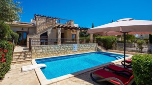 A swimming pool with stone walls, a stone staircase, and a covered seating area with umbrellas.
