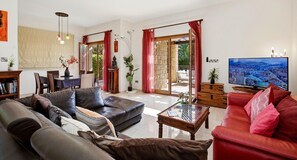 Un salón amplio con un sofá rojo, un sofá de cuero negro y una televisión que muestra un paisaje urbano.