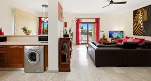 A modern living space with a kitchen, a washing machine, a sofa, and a television.
