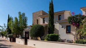 A residential street with houses featuring stone facades, a well-maintained lawn, and a clear blue sky. - Villa HG24 Cardia - Three Bedroom Villa, Sleeps 6 (Kouklia)