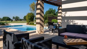 An outdoor patio with wicker furniture, a stone pillar, and a pool. - Villa HG24 Cardia - Three Bedroom Villa, Sleeps 6 (Kouklia)