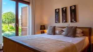 A bedroom with a large bed, a nightstand, a lamp, and three paintings on the wall. - Villa HG24 Cardia - Three Bedroom Villa, Sleeps 6 (Kouklia)
