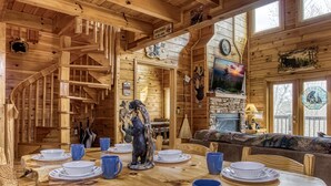 A wooden cabin interior with a dining table set for six, a fireplace, and a spiral staircase. - Located 1.5 mi. from the Parkway in Pigeon Forge. (Pigeon Forge)