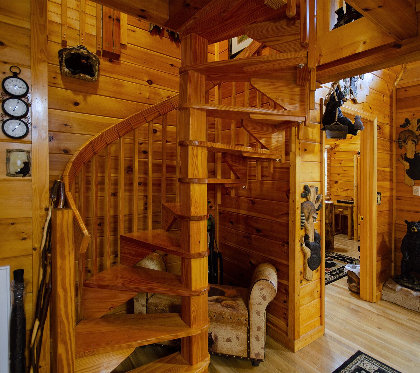 A wooden spiral staircase in a cabin with a rustic interior, including a carved wooden headboard and a clock on the wall.