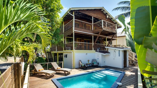 Un edificio de dos pisos con una terraza de madera, una piscina y mobiliario exterior.