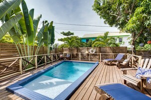Terraza de madera con piscina, sillones de descanso y plantas tropicales.