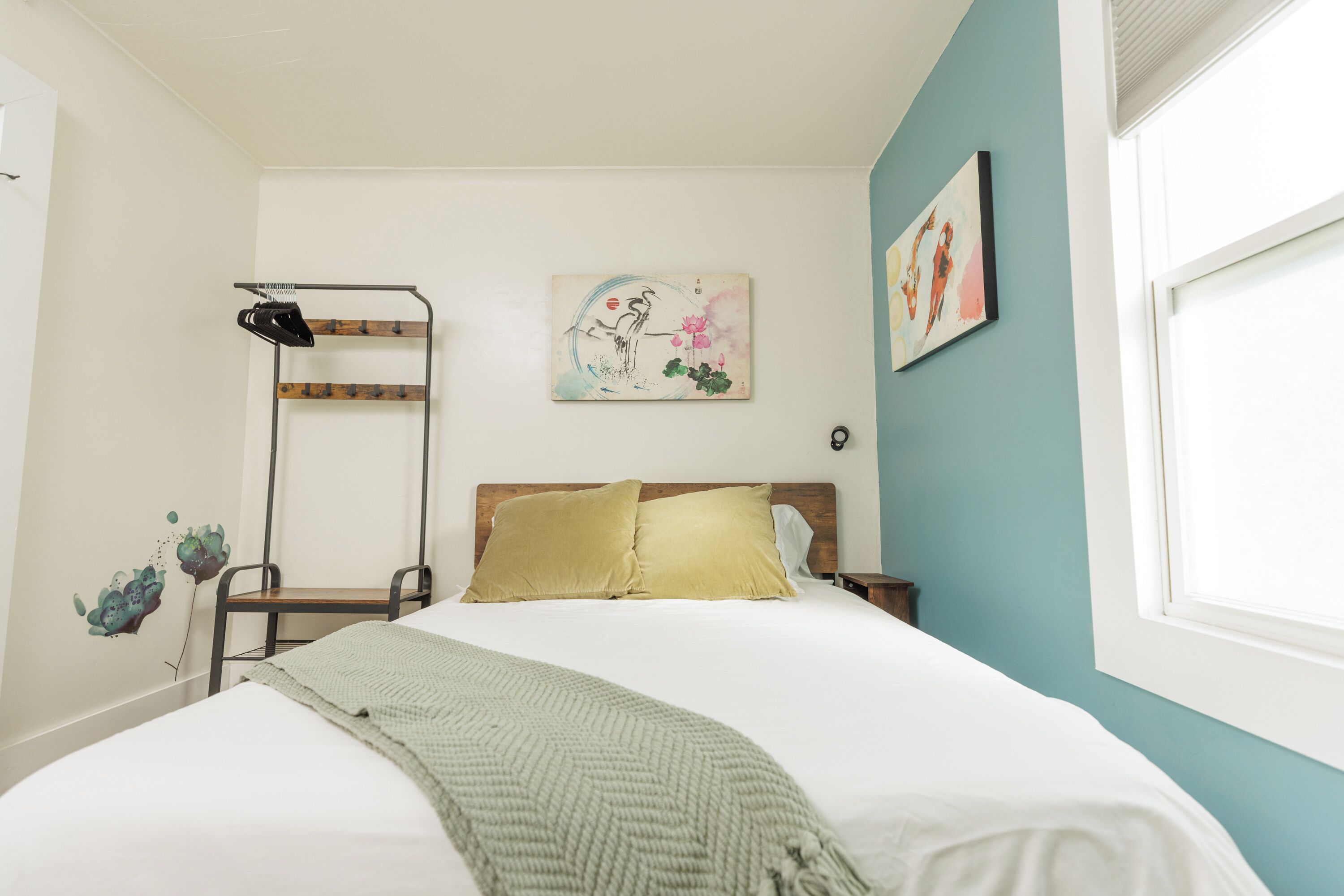 A bedroom with a bed, a wooden headboard, a wall-mounted shoe rack, a painting, and a window.