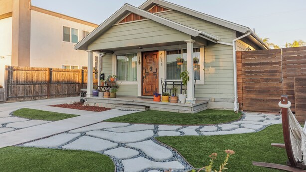 A house with a front porch, a wooden door, and a number '45771' on the door. There is a wooden fence to the right and a paved driveway leading to the house.