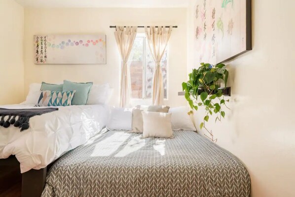 A bedroom with a bed, pillows, a bedside plant, and a window with curtains. - Private Cozy Clean, close to EVERYTHING (San Diego)