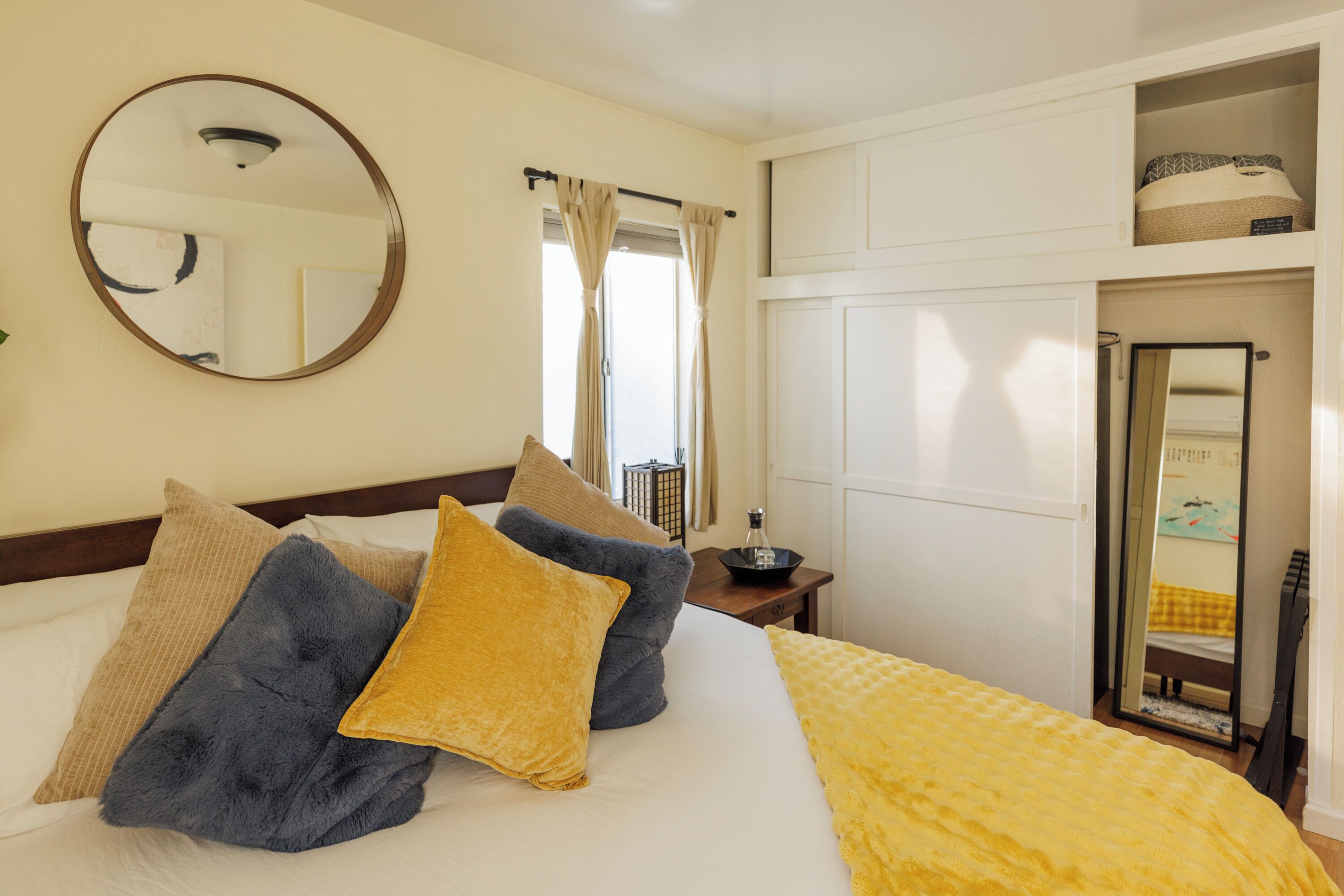 A hotel room with a bed, a mirror, a nightstand, and a window with curtains.