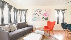 Un salón con un sofá gris, una mesa de centro blanca, un sillón rojo y un cuadro en la pared.