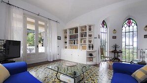 A living room with a blue sofa, a glass coffee table, a bookshelf, and a TV. - AMORE RENTALS - Villa Angelo with Private Terraces, Parking and Air Conditioning (Sant´Agnello)