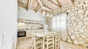 A kitchen with stone walls, wooden ceiling beams, and a dining table with chairs.