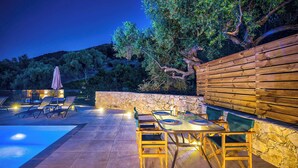 An outdoor pool area with a stone wall, wooden deck, and lounge chairs.