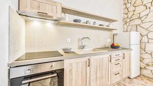 A modern kitchen with wooden cabinets, a built-in oven, a stainless steel range hood, and a stone wall.