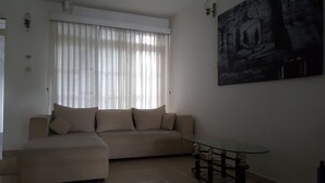 Una sala de estar con un sofá color beige, una mesa de centro de cristal y una estatua de Buda en la pared.