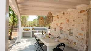 Un espace de restauration en plein air agrémenté d’un mur en pierre, d’une longue table et de luminaires suspendus en osier.