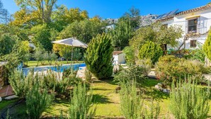 Une piscine entourée d’une végétation luxuriante et un bâtiment blanc doté d’un toit recouvert de tuiles.
