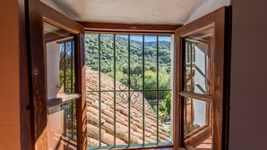 Une porte en bois ouverte, surmontée d’un portail en métal, donne accès à une terrasse dotée d’un toit en tuiles et offrant une vue sur un paysage verdoyant.