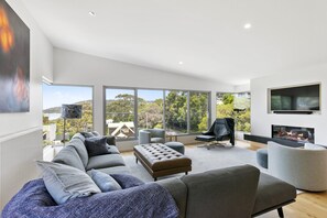 Una sala de estar moderna con un sofá modular, una chimenea y ventanas grandes que ofrecen vistas a árboles y colinas.