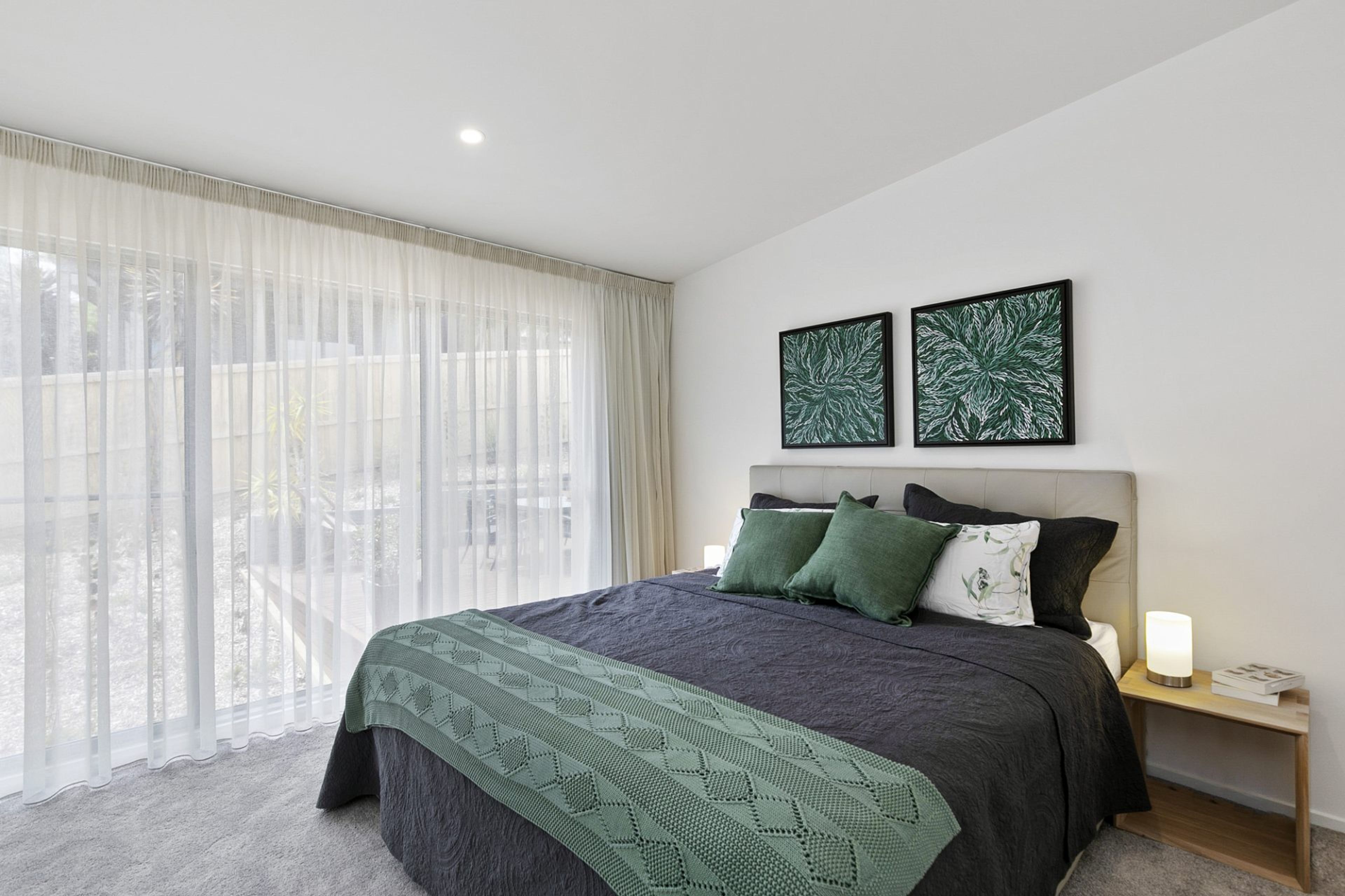 A modern bedroom with a large bed, a bedside table, and two wall-mounted artworks.