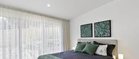 A modern bedroom with a large bed, a bedside table, and two wall-mounted artworks.