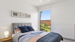 A bedroom with a bed, a nightstand, a window, and three framed pictures on the wall. - Seahaven - Brilliant Location, Stunning Modern Features (Lorne)