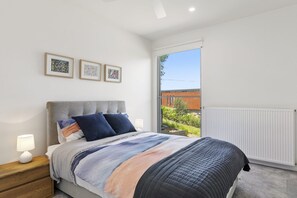 A bedroom with a bed, a nightstand, a window, and three framed pictures on the wall. - Seahaven - Brilliant Location, Stunning Modern Features (Lorne)