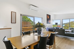 Een moderne eetruimte met een houten tafel en stoelen, een vaas met bloemen en uitzicht op het omliggende landschap door grote ramen.