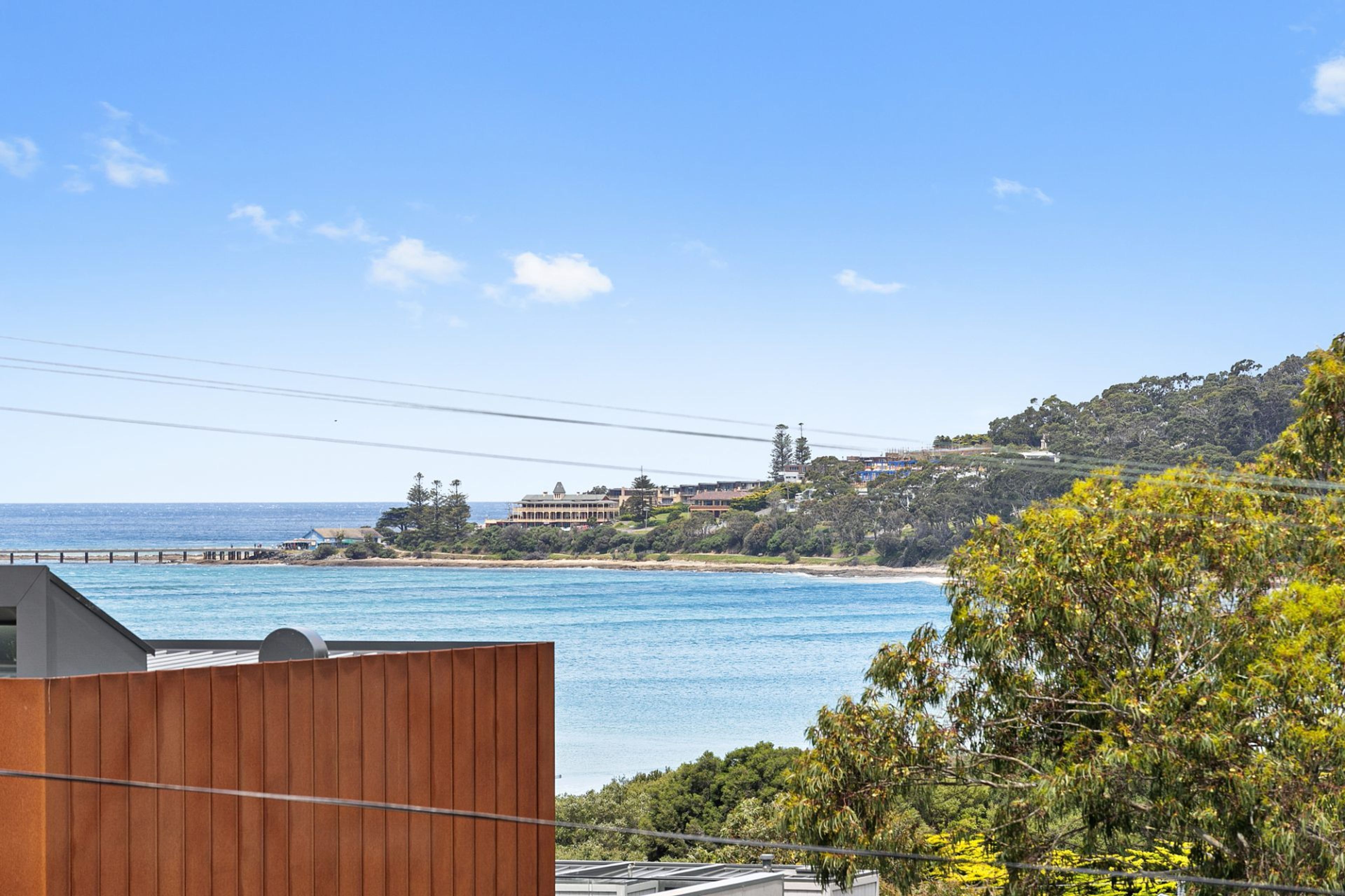 A coastal view with a wooden building in the foreground, a beach, and a hillside with buildings.