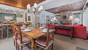 Un comedor amplio con una mesa y sillas de madera, una araña y un sofá rojo al fondo.