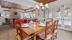 Un comedor con una mesa de madera dispuesta para seis personas, rodeada de sillas de madera con asientos acolchados. Un candelabro cuelga sobre la mesa, y la habitación tiene una pared de acento de piedra.