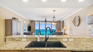 Cozinha com bancadas de granito, pia preta e vista para o mar.