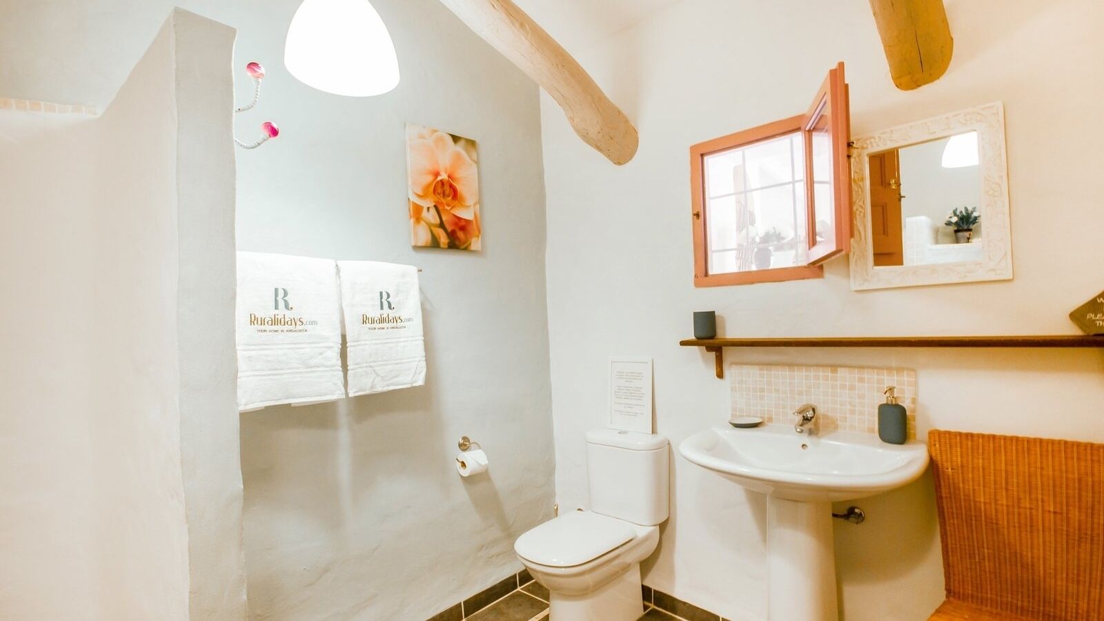 A bathroom with a toilet, sink, and towel rack. There are towels hanging on the wall and a picture of flowers.
