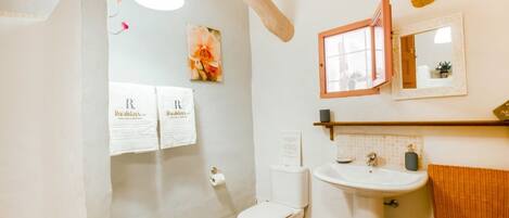 A bathroom with a toilet, sink, and towel rack. There are towels hanging on the wall and a picture of flowers.