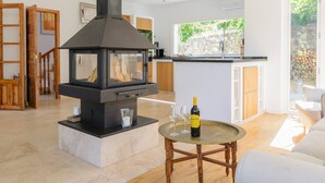 A modern kitchen with a wood-burning stove, a dining area with a round table, and a view of the outdoors through a large window. - Villa Valparaiso Alhama de Granada by Ruralidays (Granada)
