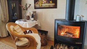 Een gezellige kamer met een rieten stoel, een tafel met een vaas en een wijnfles, en een houtkachel.