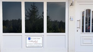 Een wit gebouw met grote ramen en een deur met een ruit. Op de ramen staat een bordje met de tekst "P für unsere Gäste Feldbergblick LANDHAUS-APPARTMENT www.feldbergblick-st-maergen.de".